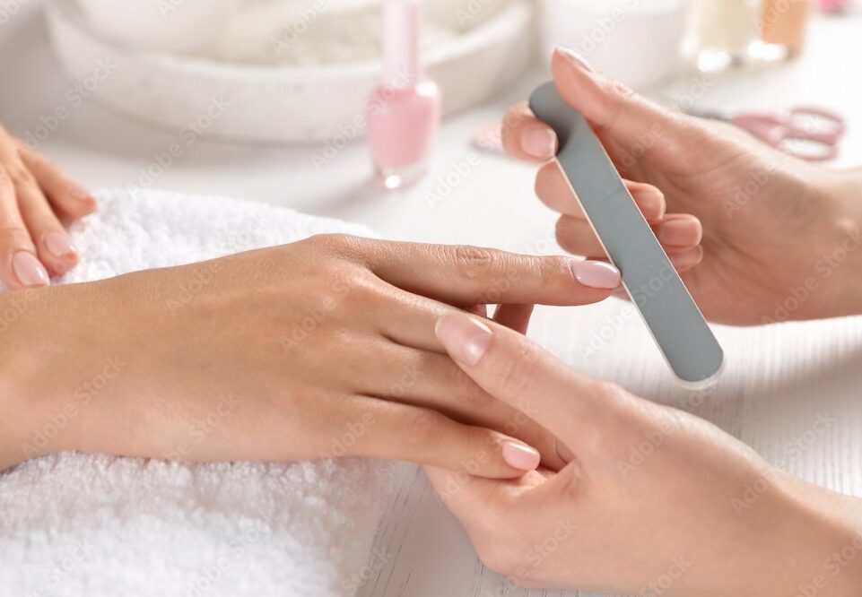 Manicurist filing client's nails at table, closeup. Spa treatment